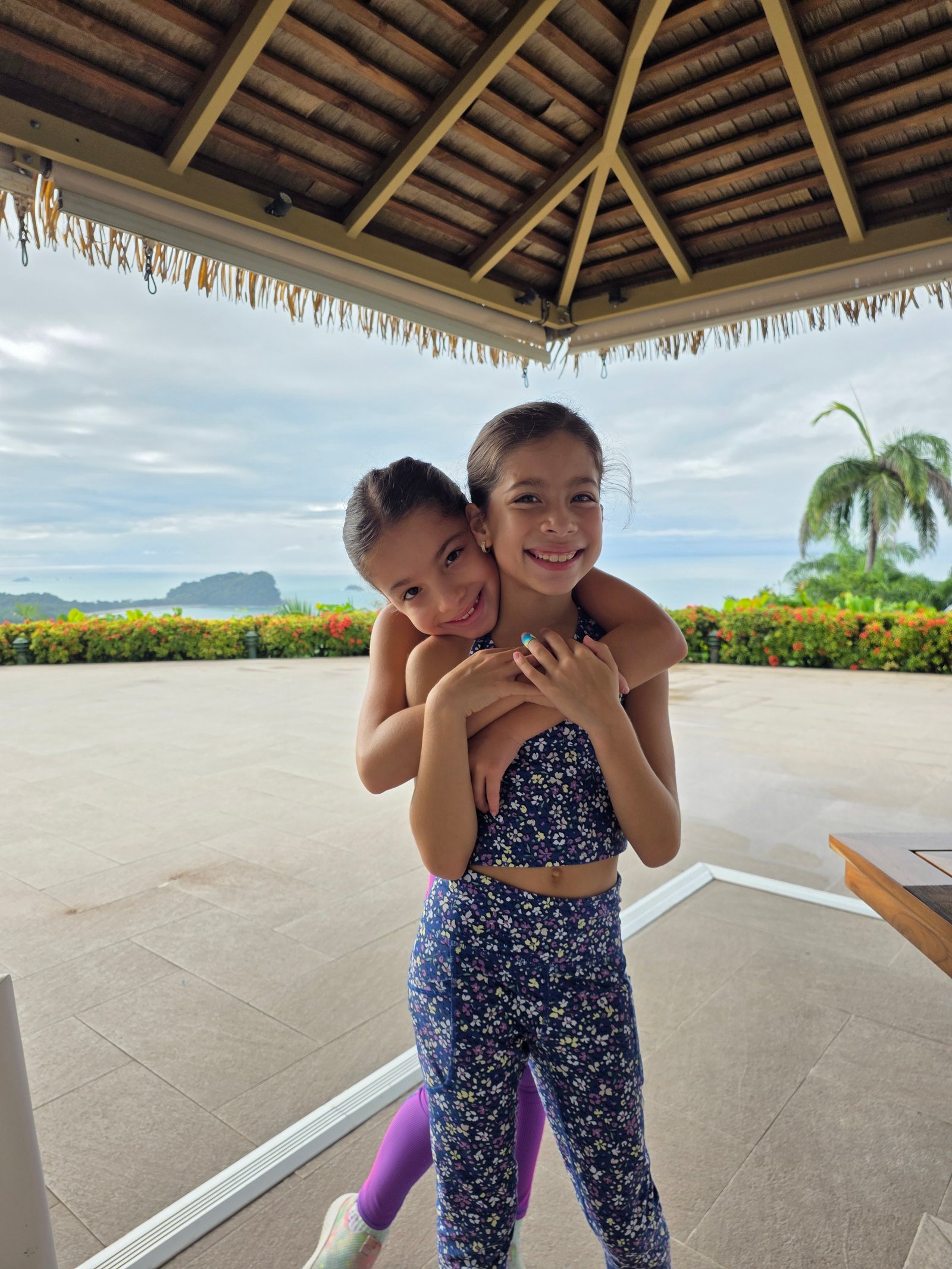 Both girls piggyback hug with ocean and islands in background