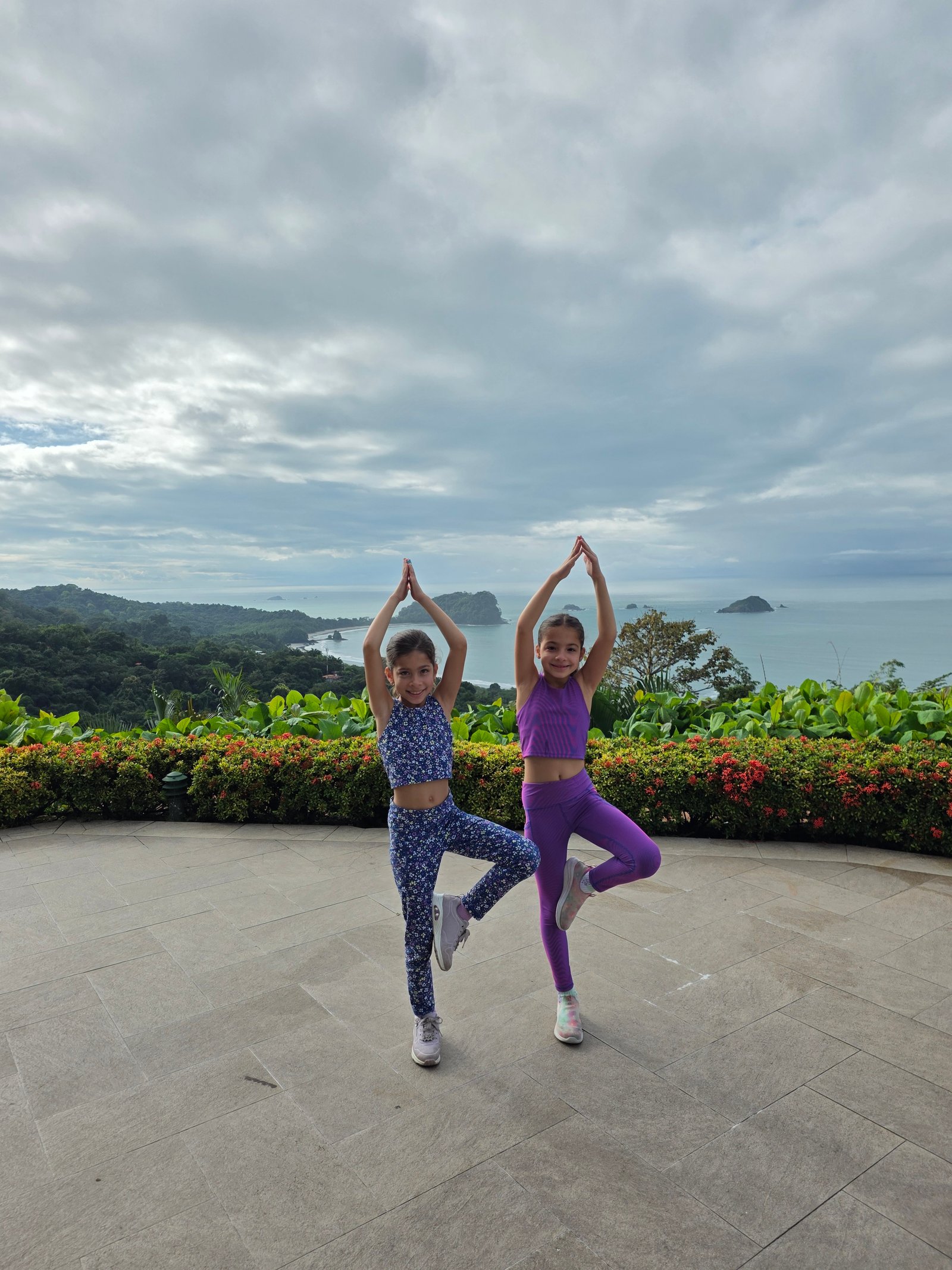 Both girls doing yoga tree pose with ocean panorama behind them